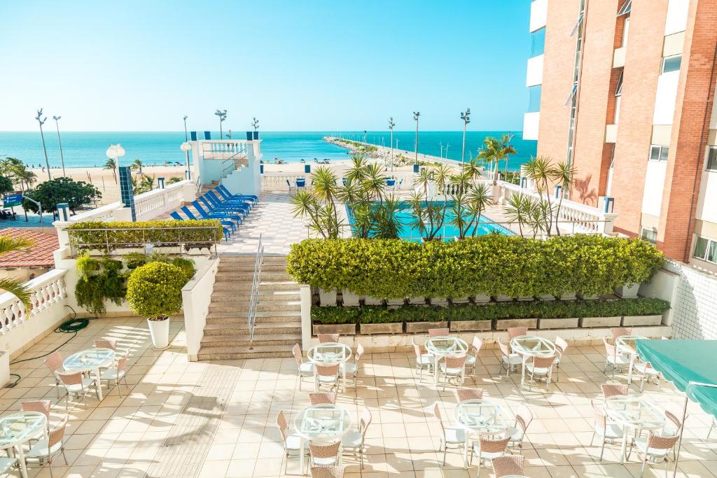 Pátio externo do hotel com mesas e cadeiras, área da piscina e vista para o oceano sob um céu azul claro, na propriedade do Hotel Sonata de Iracema na Praia de Iracema.