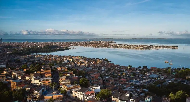 Vista aérea de uma cidade costeira com prédios densamente povoados, águas calmas e uma península sob um céu azul.