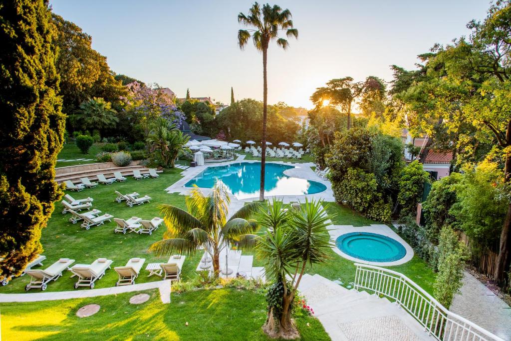 Extenso jardim do Olissippo Lapa Palace – The Leading Hotels of the World comuma piscina cercada por espreguiçadeiras e árvores, para representar hotéis de luxo em Lisboa