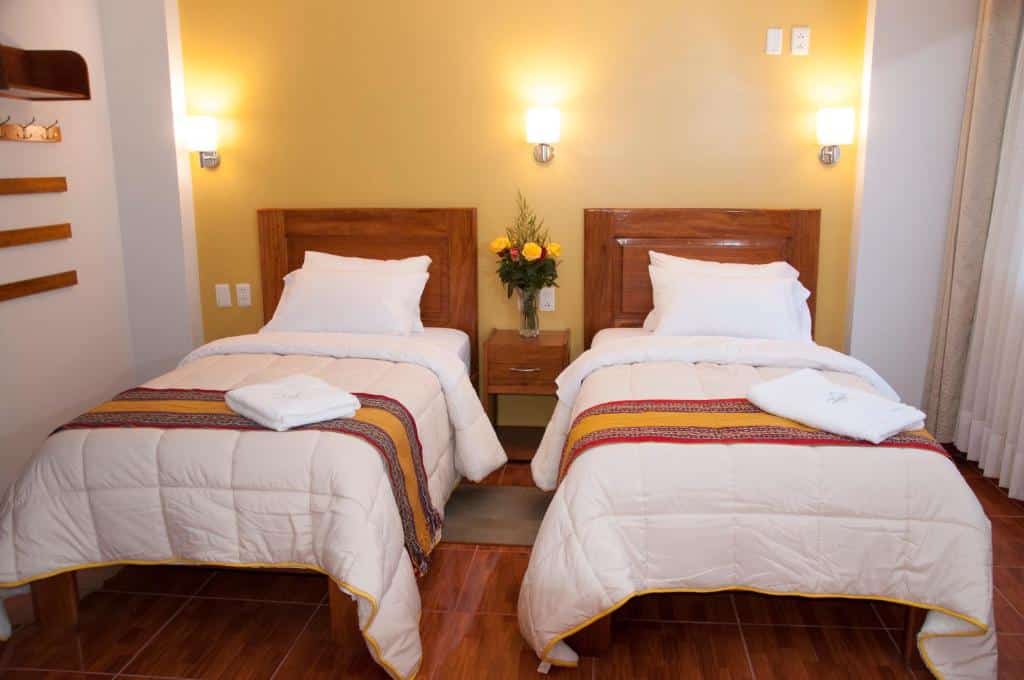 duas camas de solteiro no quarto do Picos House dispostas lado a lado. Há uma toalha branca dobrada em cima da cama, que está coberta por uma manta grossa
