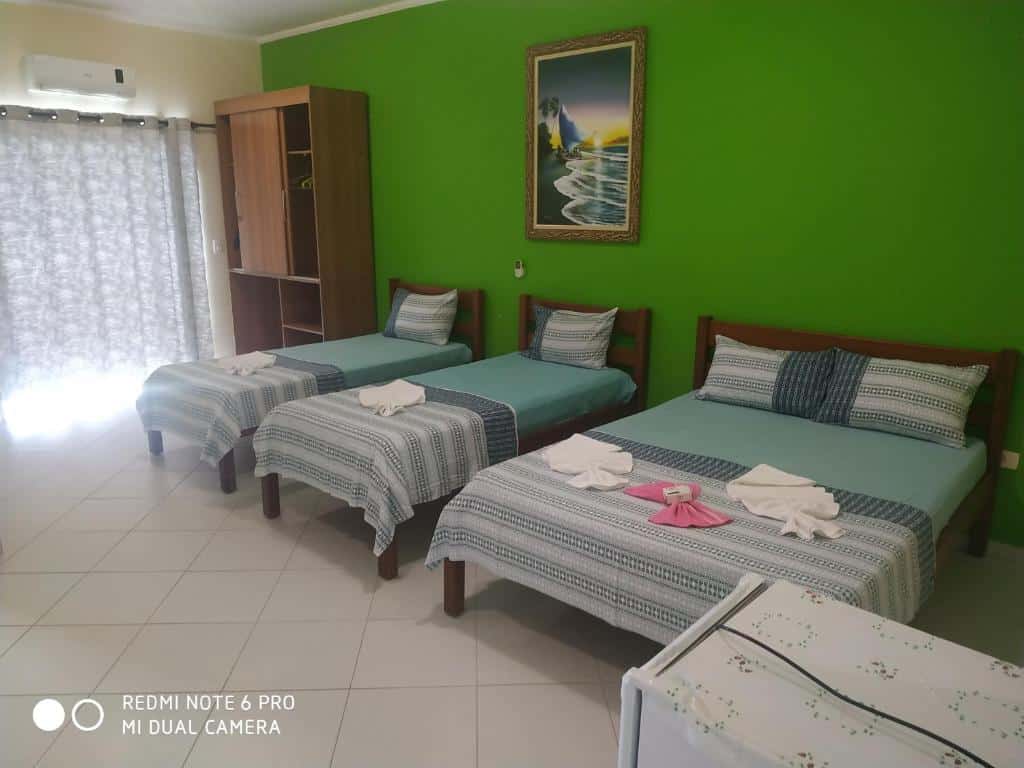 Quarto com parede verde, guarda-roupa, duas camas de solteiro e uma cama de casal na Suítes Ubatuba