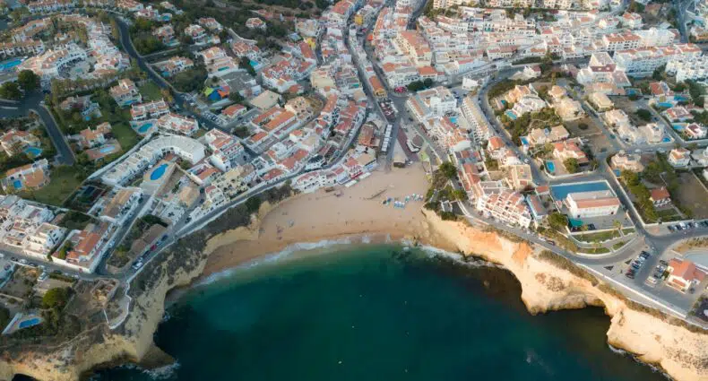 Vista aérea de uma cidade litorânea com praia de areia, água azul-turquesa e edifícios densamente povoados com telhados de telhas vermelhas.