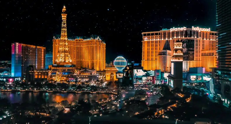 A foto mostra uma visão geral da Strip durante à noite. Todos os hotéis estão ilminados. Do lado esquerdo está a torre eiffel e, no meio, o balão do Paris Las Vegas. A imagem é capa no post de onde ficar em Las Vegas.