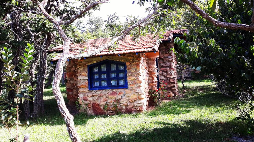 chalé de pedra na Pousada Casa do Arco na Lapinha da Serra com muita grama e árvores ao redor. Na frente da casa é possível ver uma janela pintada de azul royal
