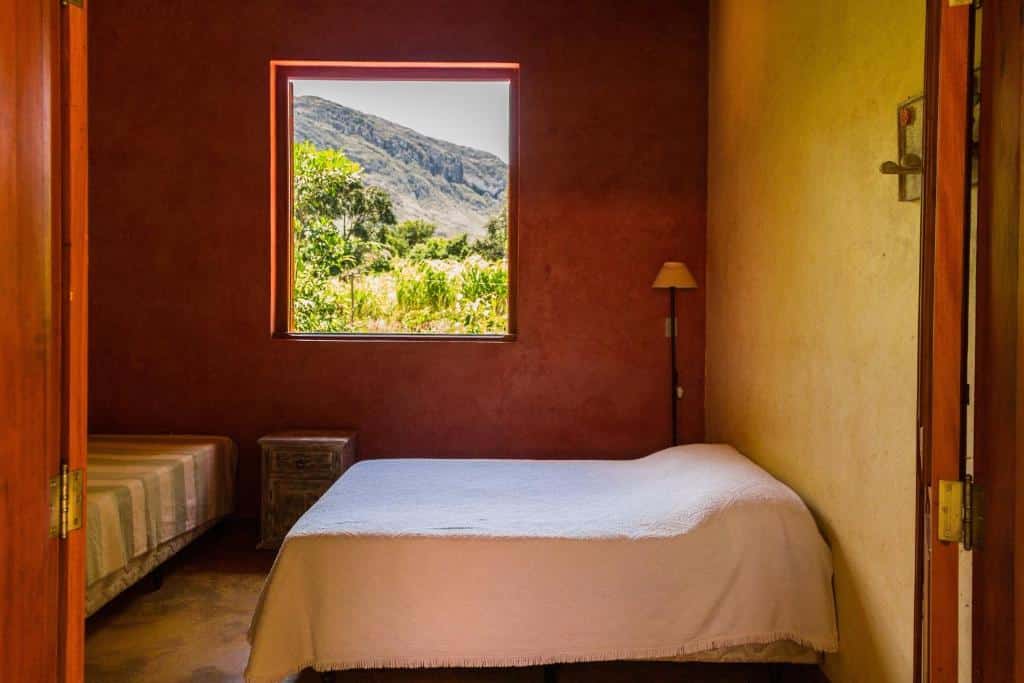quarto da Pousada Opicodocipo com duas camas de casal e uma janela com vista para as montanhas na Lapinha da Serra