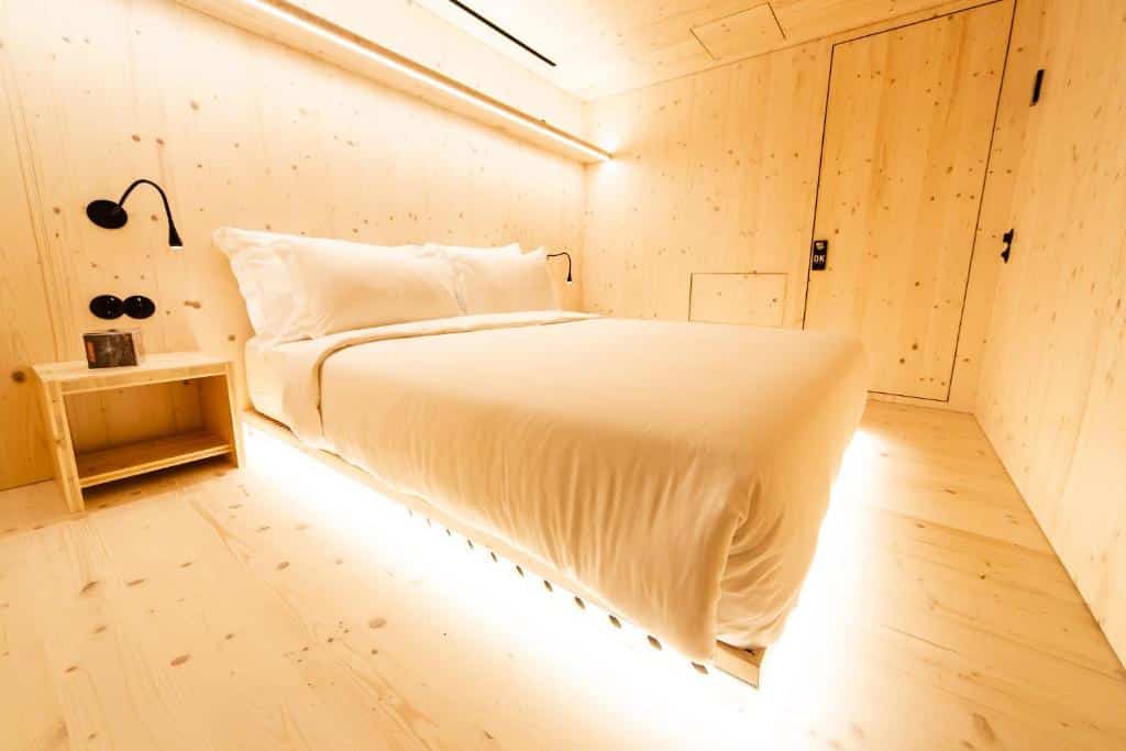 Quarto do Zero Box Lodge Porto com cama de casal do lado esquerdo no centro do quarto e do lado esquerdo da cama uma cômoda com luminária. Representa melhores hotéis no Porto.