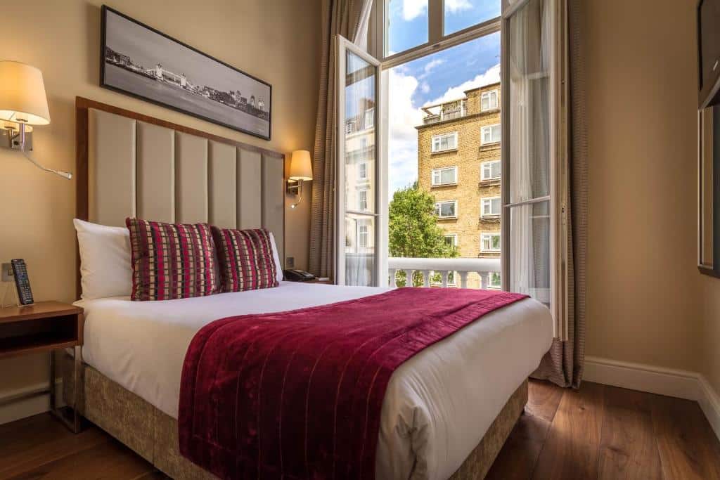 Quarto do The Belgrave Hotel com uma cama de casal, uma janela ampla com vista para a cidade, chão de madeira e duas mesinhas de cabeceira com luminárias