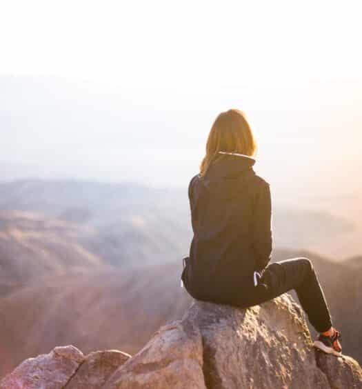 Mulher sobre rocha observando paisagem - capa do post Coris Seguro Viagem