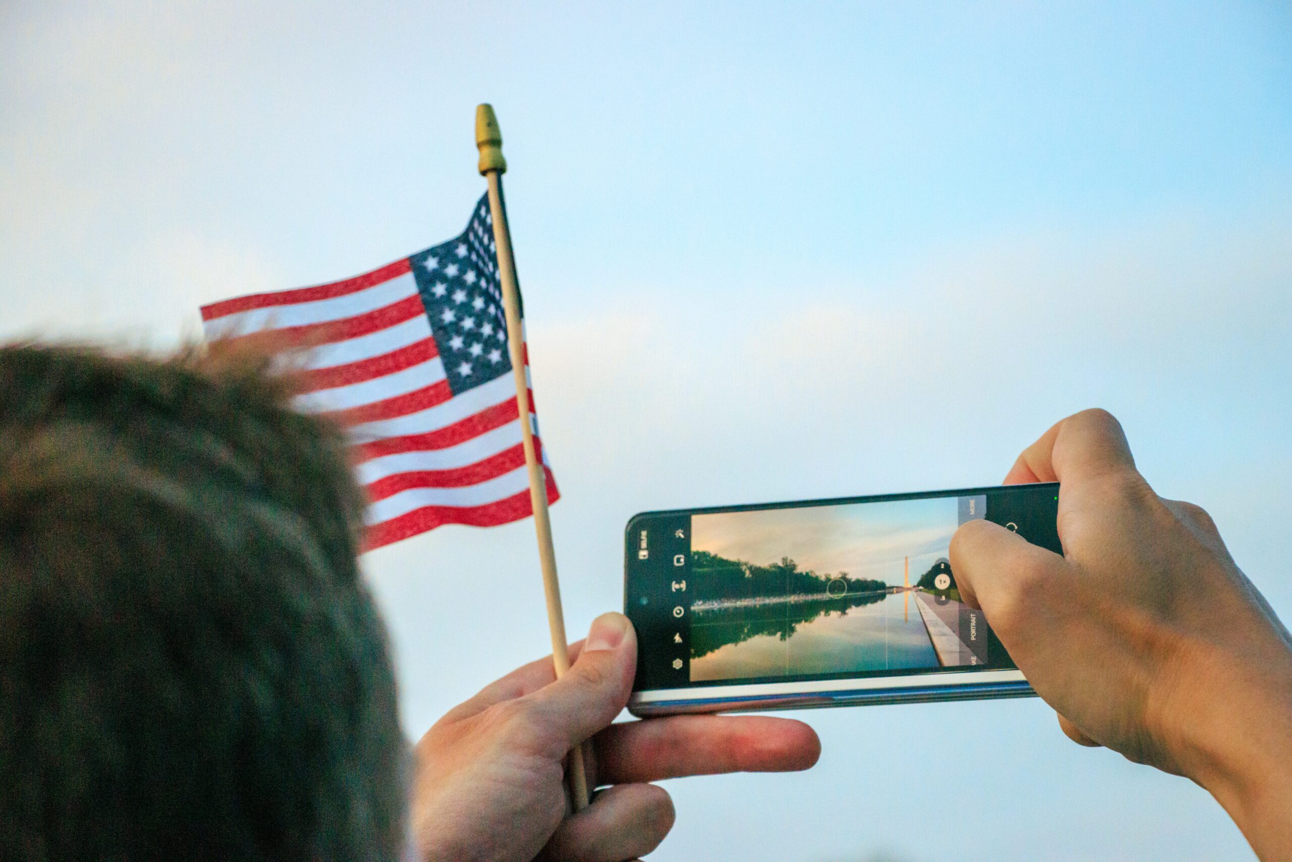 garoto tirando foto com o celular do obeslico em washington dc enquanto desegura um apequena bandeira dos EUA