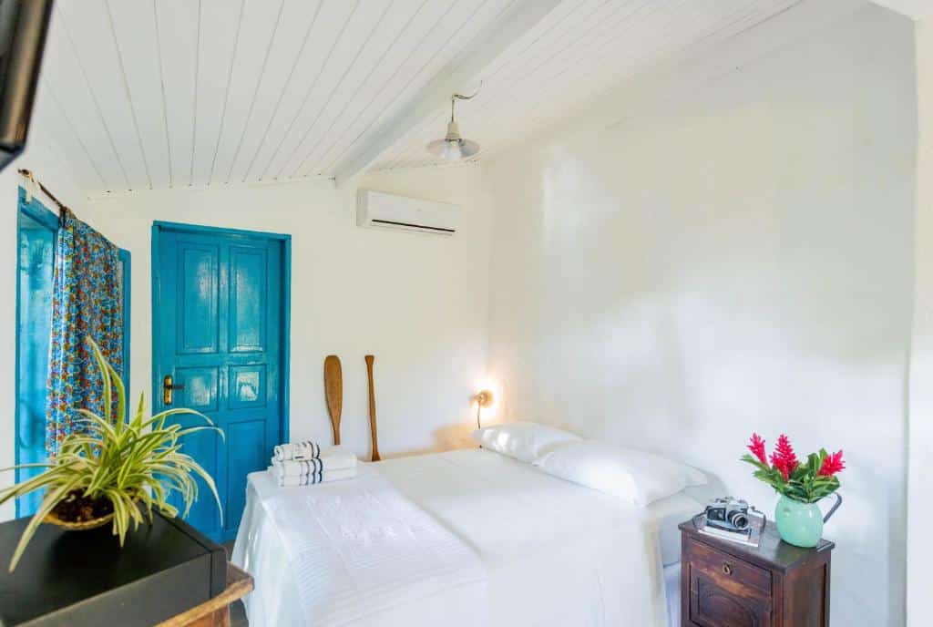 Quarto todo branco na Ilhabela Homestay, com porta azul, cama de casal e ar-condicionado