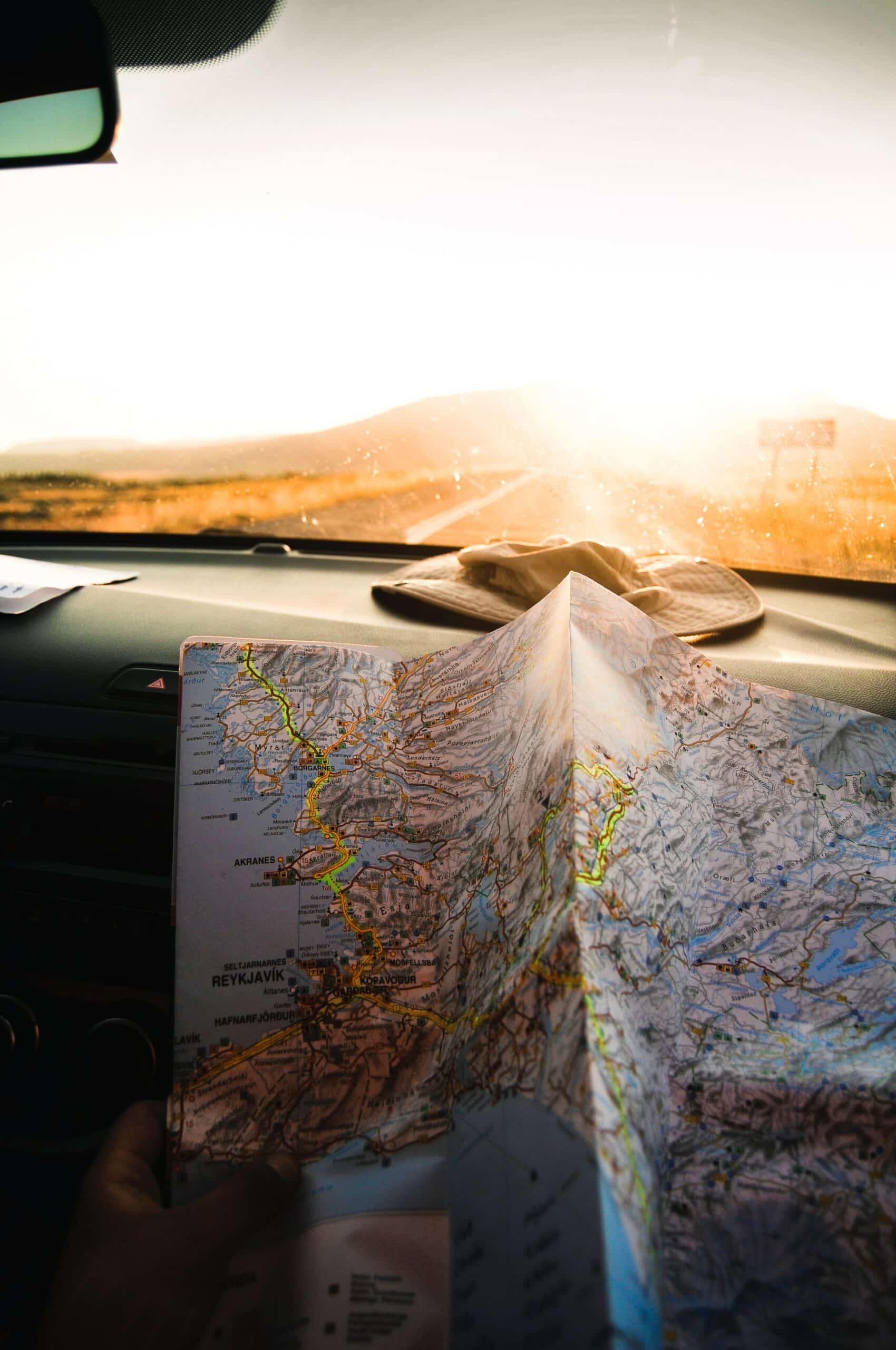 pessoa segurando um mapa dentro de um carro com vista para estrada no pôr do sol