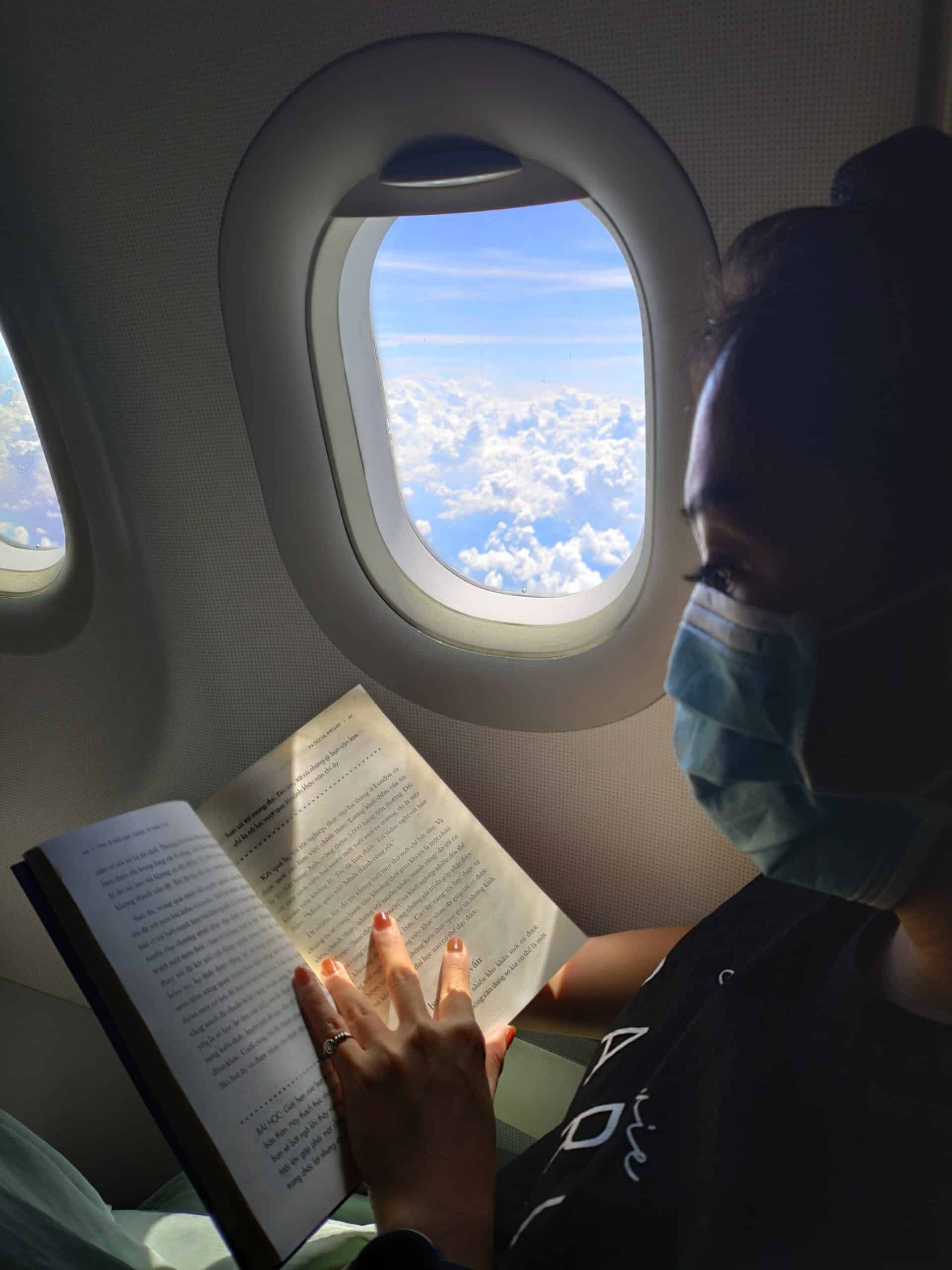 mulher lendo um livro usando máscara para viajar de avião