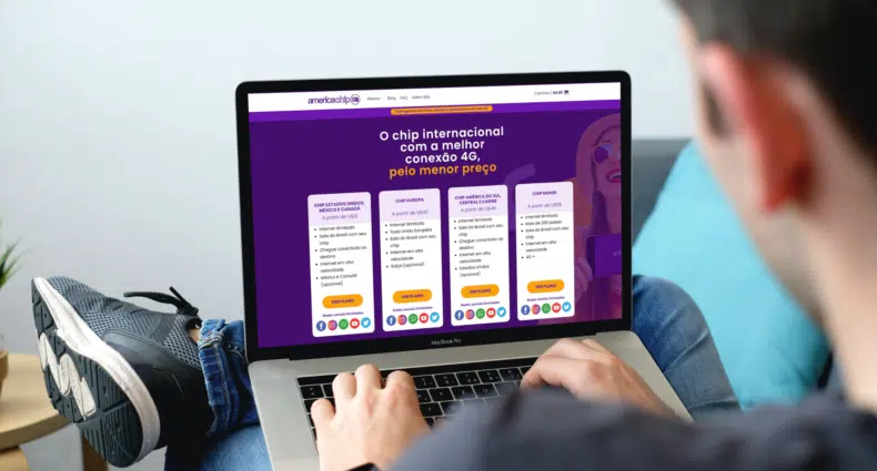 homem com um notebook aberto sobre as pernas dobradas, a tela do computador mostra a página inicial do site america chip