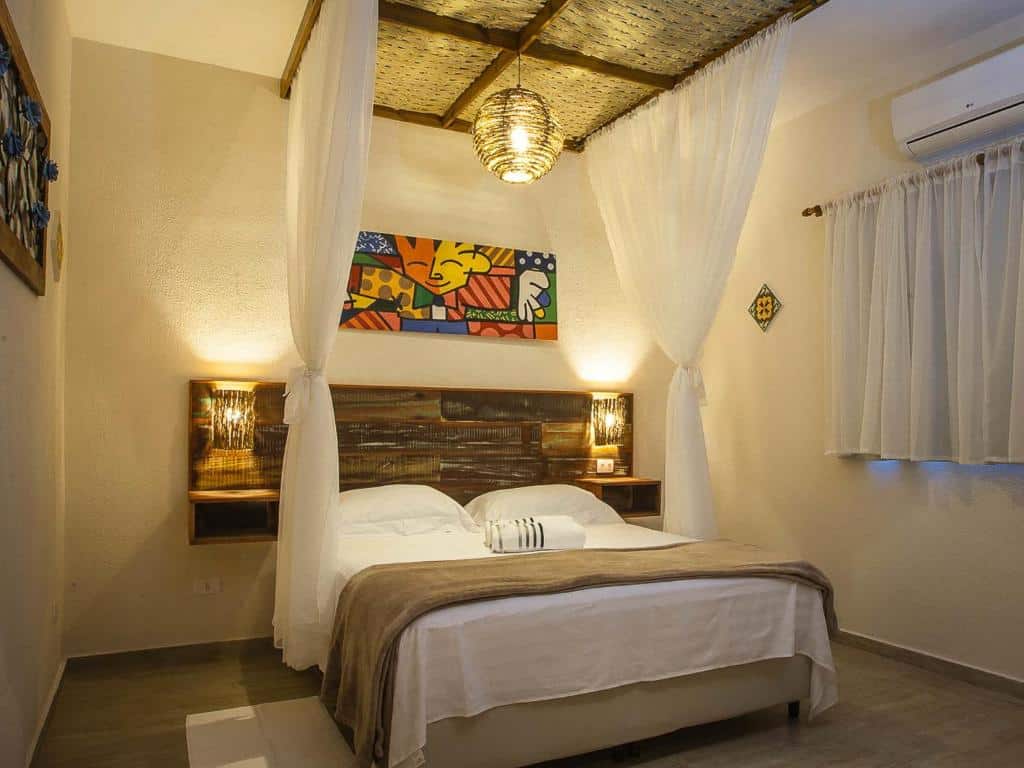 Quarto da Pousada de Charme Emirados, em Ilhabela, com cama de casal, mosqueteira, quadro decorativo e luzes de cabeceira