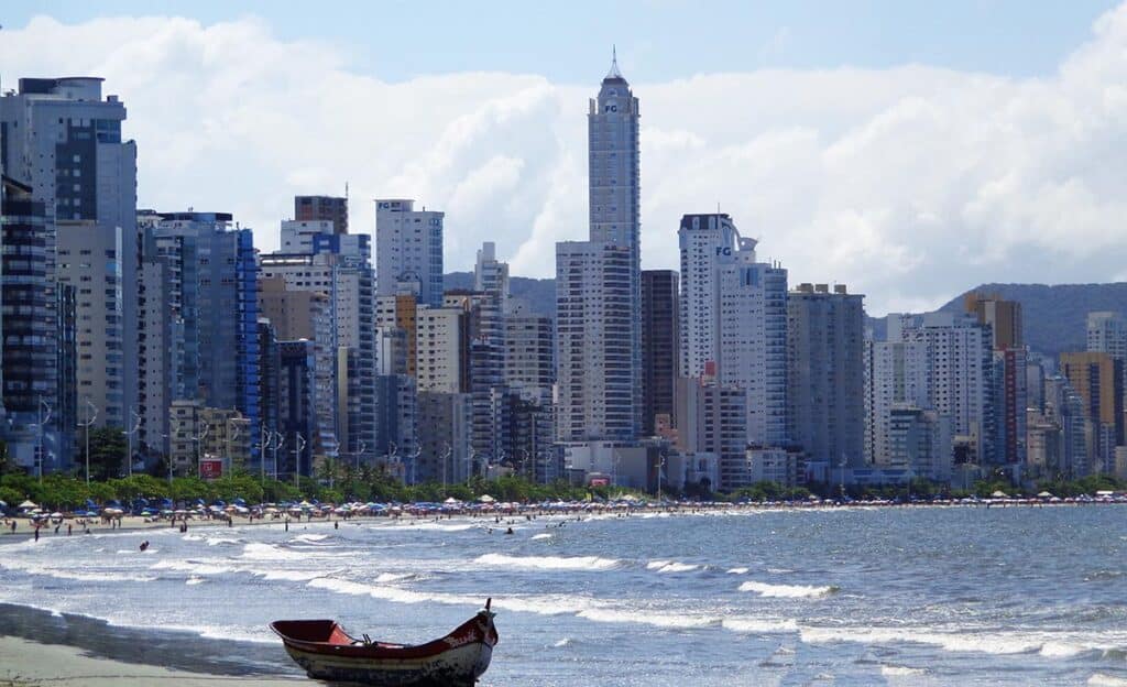 Praia rodeada por prédios e com um pequeno barco na areia em Balneário Camboriú.