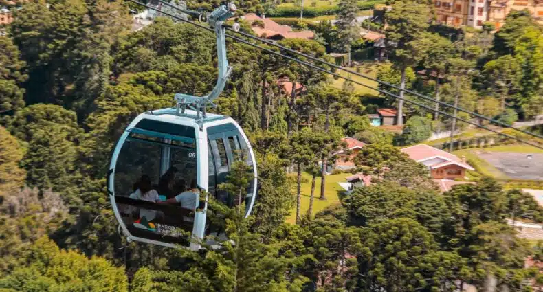 Um teleférico envidraçado com pessoas dentro, passando por entre árvores, para representar teleférico em Campos do Jordão