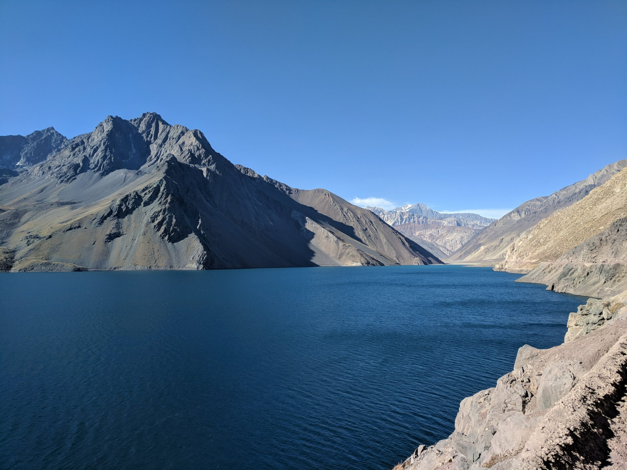 Vista do lago em Cajón del Maipo para ilustrar o post de seguro viagem Chile. Montanhas escuras cercam o local de águas azul-marinho. - Foto:  Alice Yamamura, via Unsplash