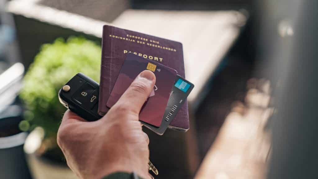Mão de homem segurando chaves do carro, passaporte e dois cartões de crédito. - Foto: CardMap via Unsplash