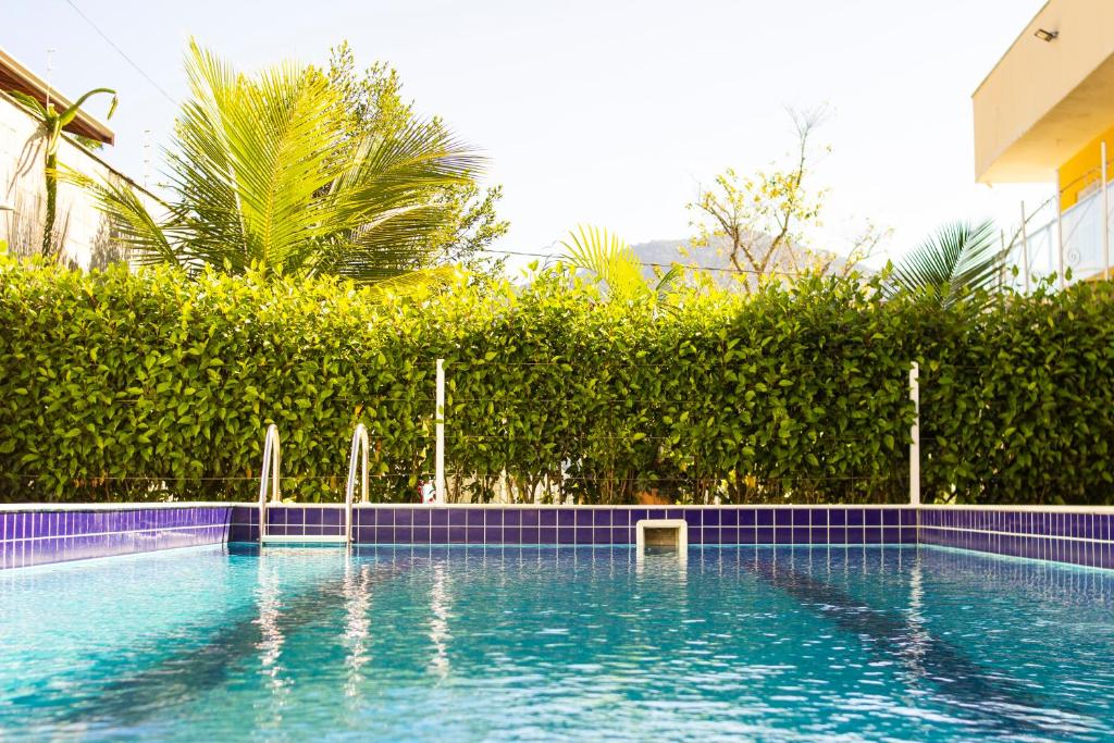 Piscina externa com azulejos azuis, escada de metal e cerca verde sob um céu claro em uma área residencial nos Chalés Mallumar na Maranduba.