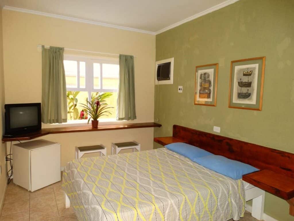 Quarto do Hotel Pousada do Sol, em Ubatuba, com paredes verdes, ar-condicionado, TV, frigobar e cama de casal