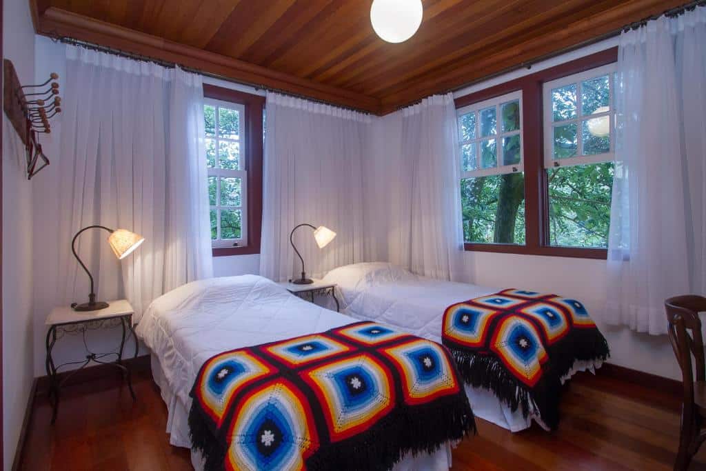 quarto da Pousada Arcádia Mineira com duas camas de solteiro e janelas amplas com vista para o jardim