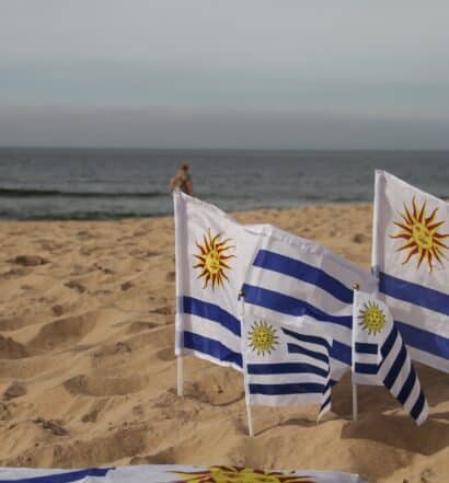 Bandeiras do Uruguai fincadas na areia à beira-mar.