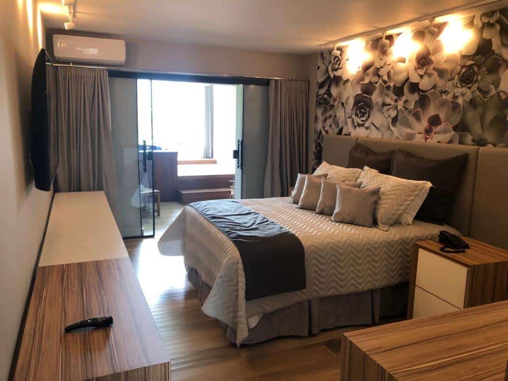 Quarto de casal do Wembley Inn Hotel, com cama alta, mesa de cabeceira, TV em frente à cama e papel de parede florido