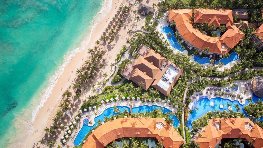 Vista aérea do Majestic Elegance Punta Cana Resort. Piscinas estão espalhadas entre os prédios do local, e há várias árvores ao redor. Do lado esquerdo da imagem está a praia.