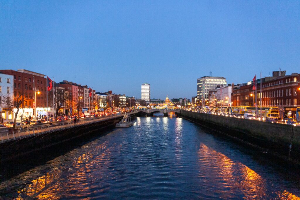 Vista do rio Liffey em Dublin, há uma pequena embarcação, e nas laterais do rio há prédios antigos e carros passando, para representar seguro viagem Dublin