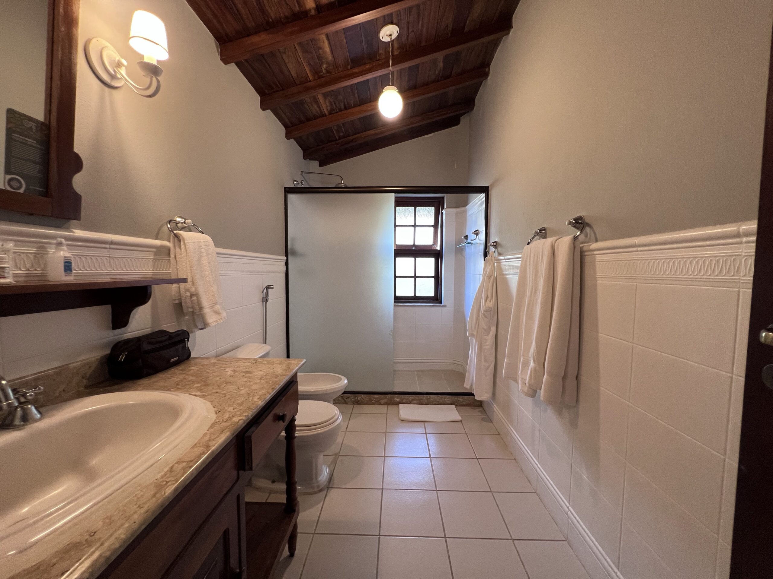 Banheiro amplo com toalhas, roupão, box espaçoso, pia larga, vaso sanitário e bidê, no Quarto Luxo do Vila Angatu