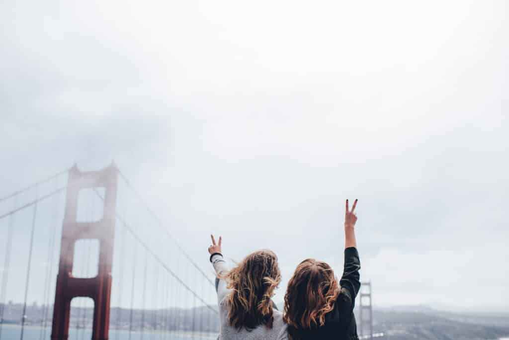 Duas mulheres fazendo sinal de paz e amor com os dedos, em frente à Golden Gate Bridge, em San Francisco