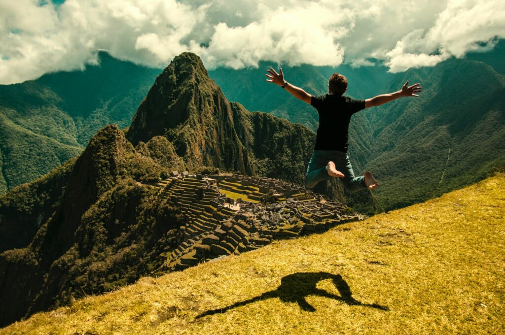 Homem pulando e olhando as ruínas incas Machu Picchu, no Peru