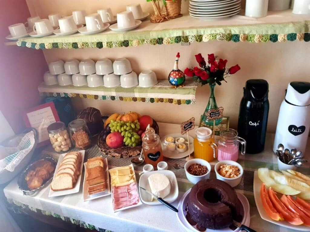 Mesa de café da manhã na Pousada Sayonara, em Atibaia com várias opções de pães, frios, sucos e bolos.