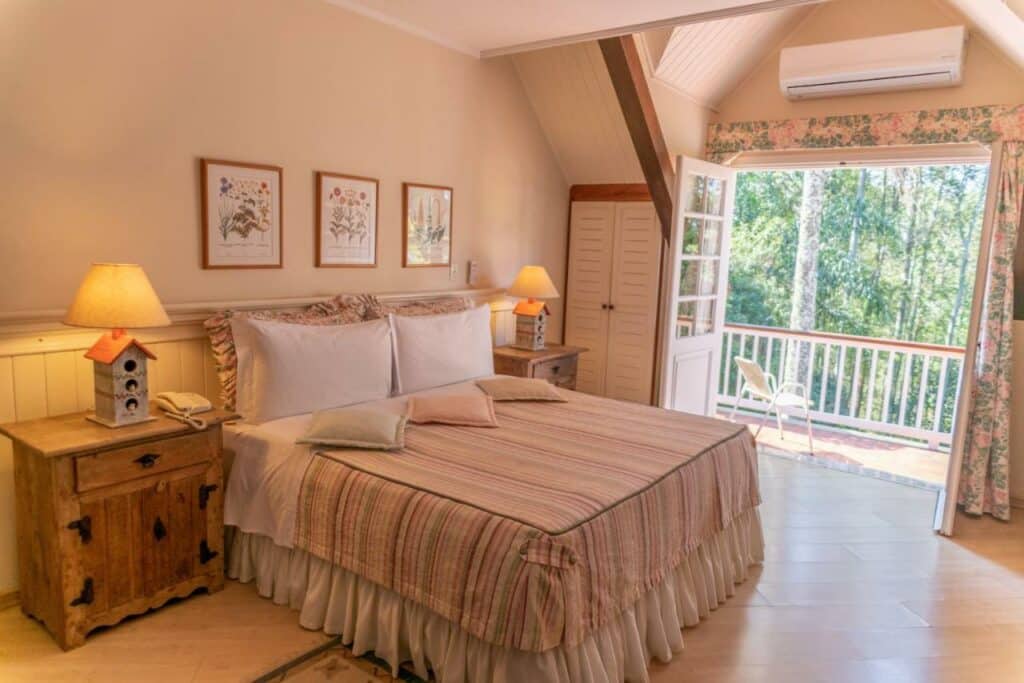 Quarto do Recanto da Paz Hotel Fazenda, com cama de casal do lado esquerdo com duas cômodas de madeira com luminária.