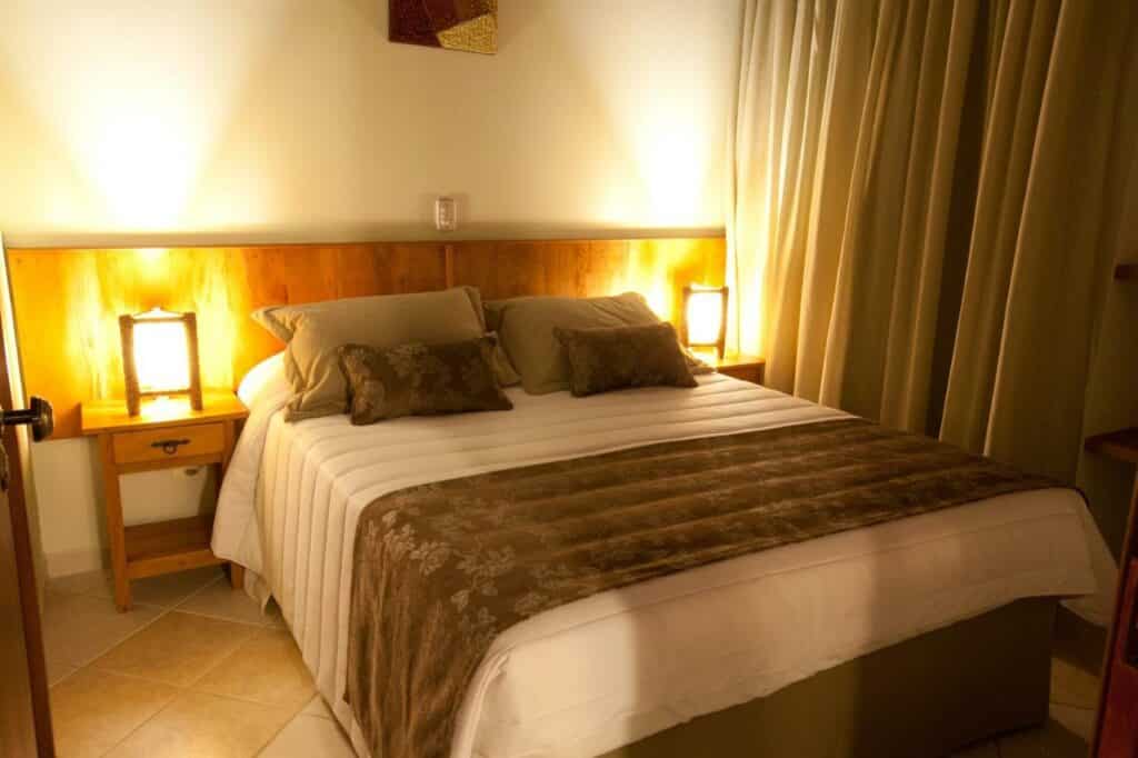 Quarto com cama de casal no Refúgio do Saci Hotel e duas luminárias de cada lado da cama.