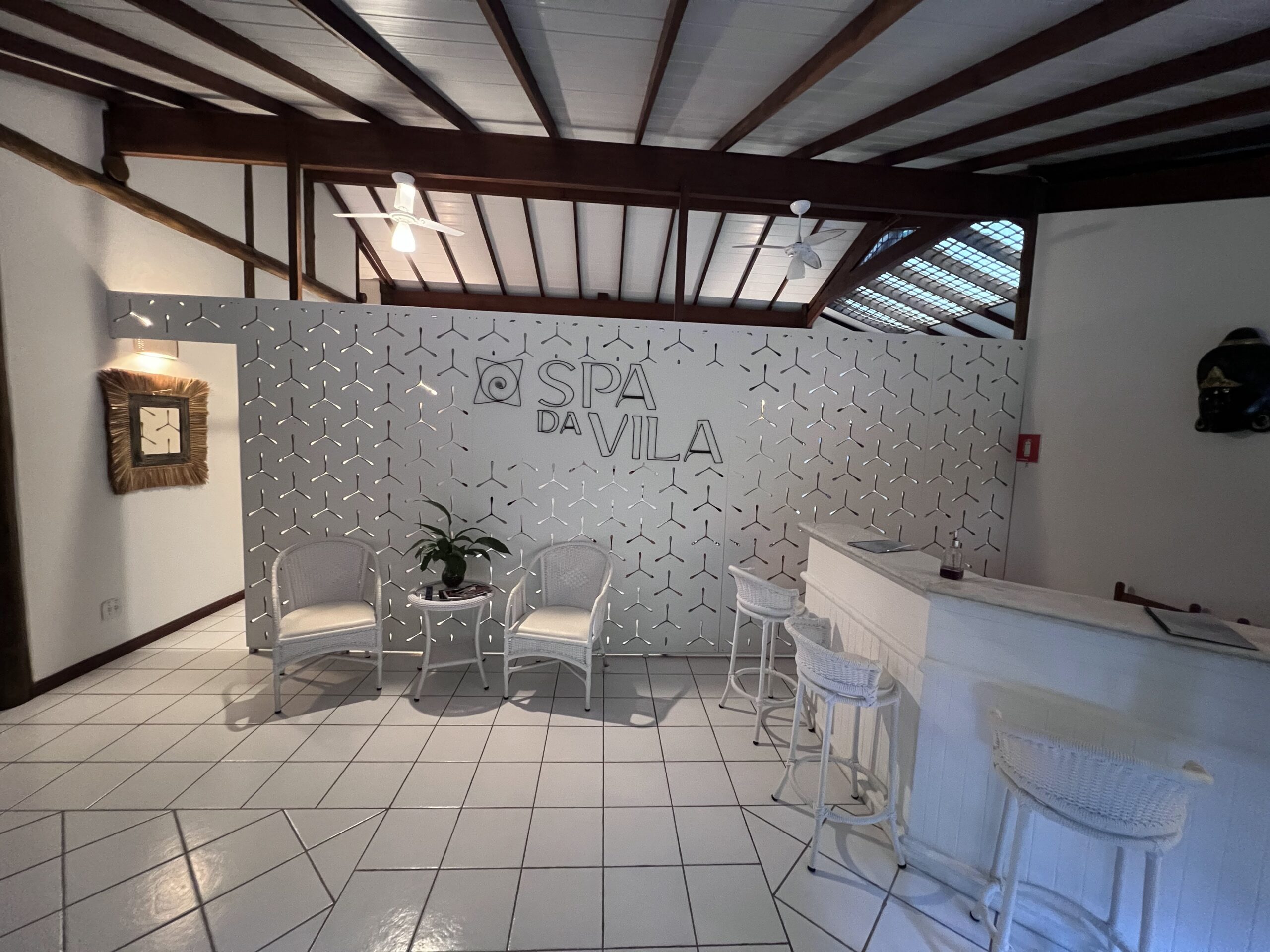 Recepção do Spa da Vila, no Vila Angatu, com balcão, banquetas e cadeiras brancas