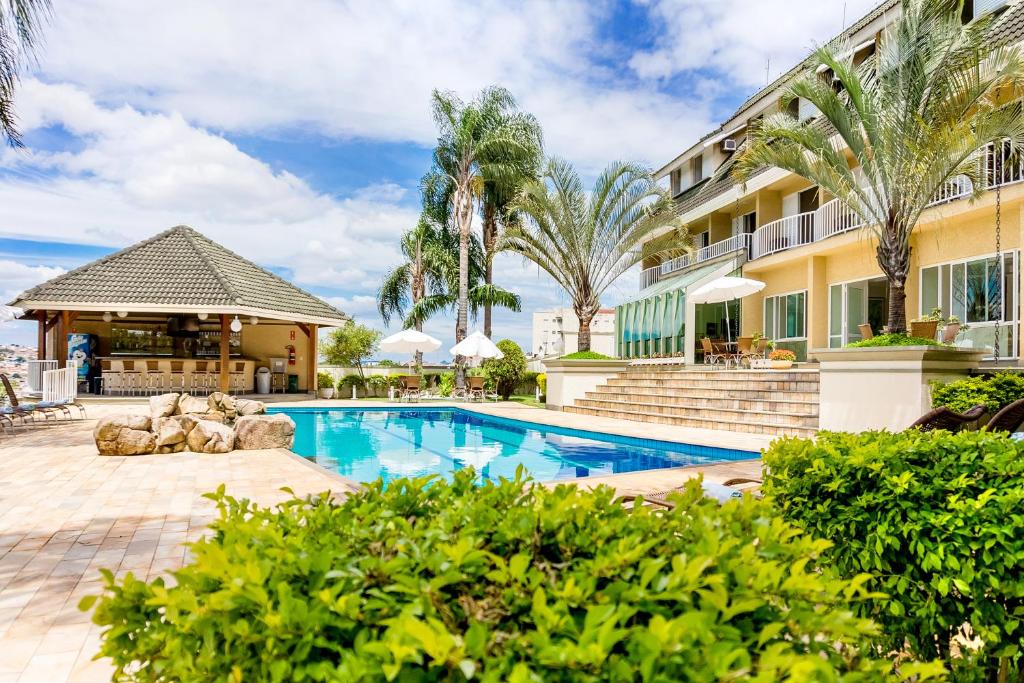 Piscina e área externa do Vila Verde Hotel durante o dia com piscina a frente e do lado esquerdo a hospedagem. Representa hotéis em Atibaia.