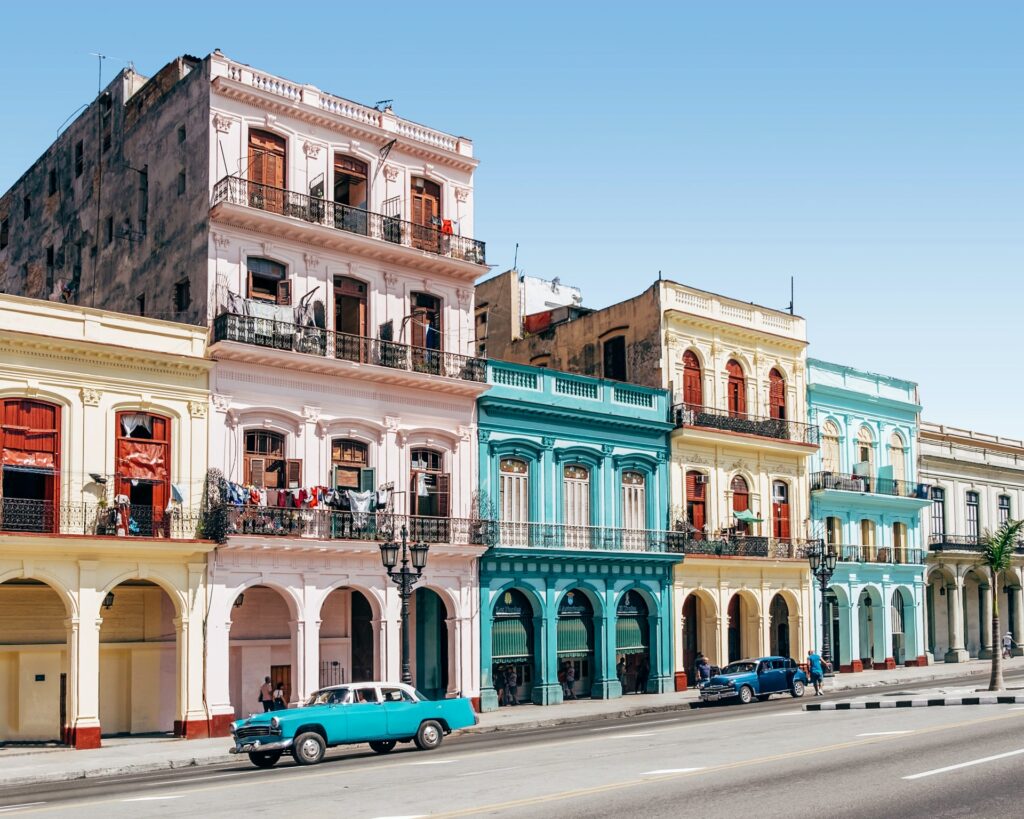 Casinhas coloridas, de arquitetura marcante, e dois carros antigos estacionados na rua de Cuba, uma das ilhas do Caribe