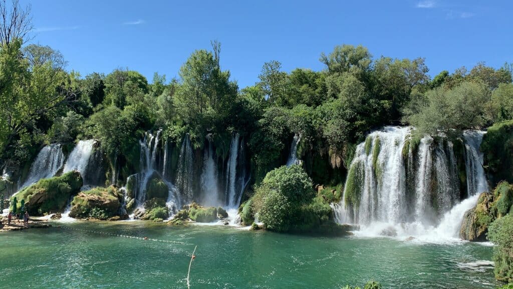 Quedas de águas da Cachoeira Kravika rodeado de muito verde e um céu azul em Bósnia e Herzegovina. Seguro Viagem Bósnia e Herzegovina.