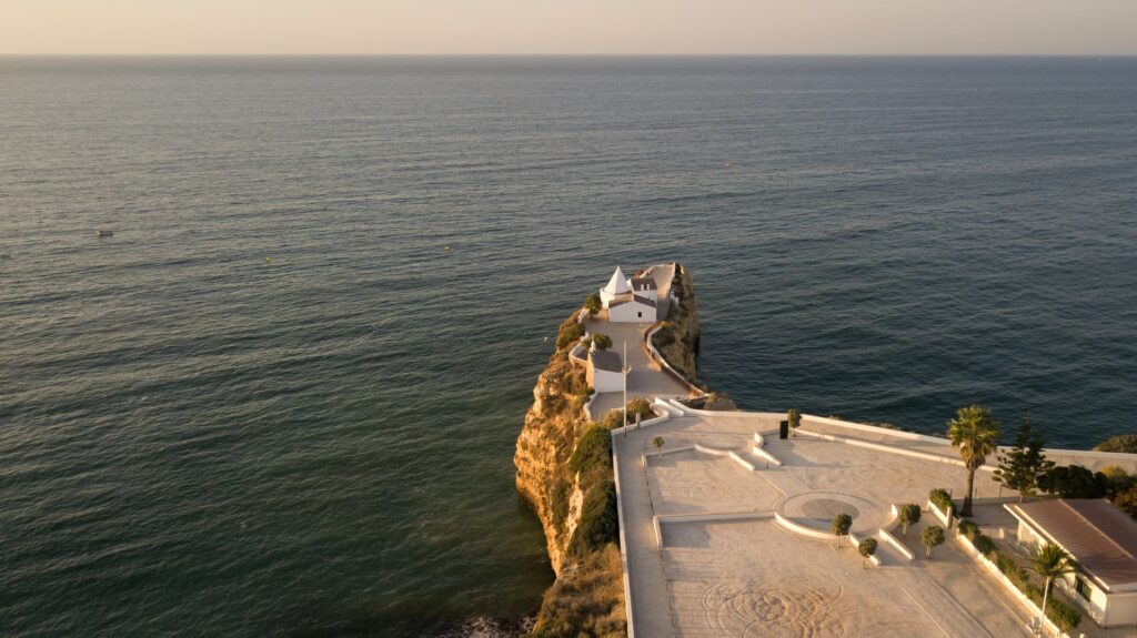 Encosta do mar do Algarde com igrejinha na ponta, ilustrando parte do post de "quanto custa seguro viagem para Portugal"