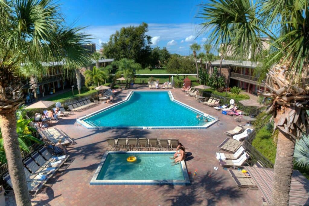 piscina do Rosen Inn International Near the Parks, um dos hotéis em Orlando, em formato de T com uma menor retangular de um lado, há cadeiras e palmeiras ao redor