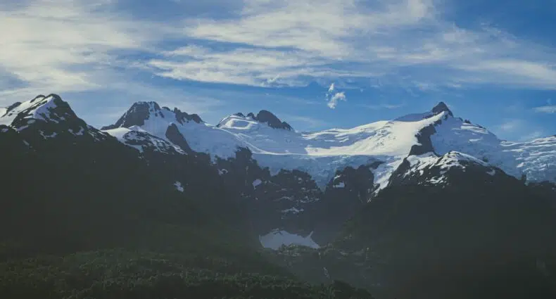 Montanhas cobertas de neve na cordilheira dos andes sob um céu azul claro, com manchas de neve e encostas escuras visíveis em primeiro plano.
