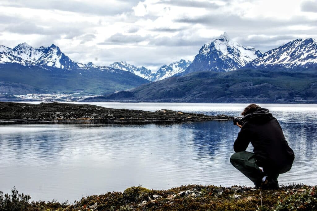 Homem com uma câmera na mão tirando foto do arquipélago Terra do Fogo na província argentina de Ushuaia, que está cercado por muitas montanhas cobertas de neve.