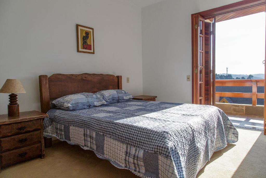 Quarto no Apartamento para temporada no Alto do Capivari, uma cama de casal, móveis em madeira, um pequeno abajur e uma sacada com vista para as montanhas, para representar airbnb em Campos do Jordão