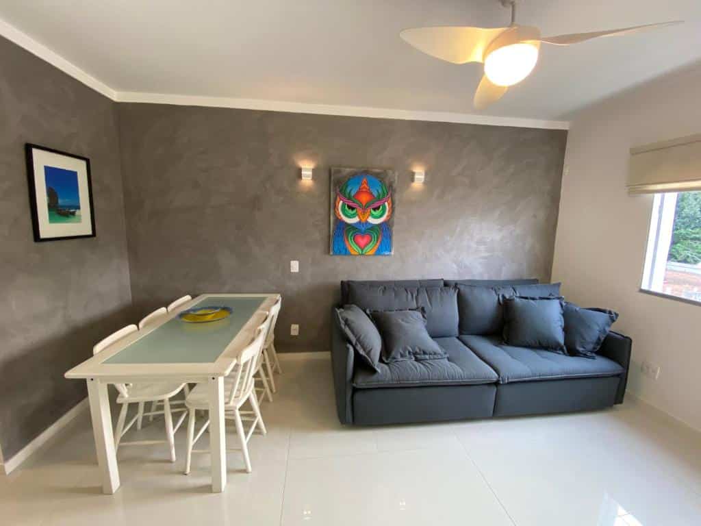 Sala de estar do  Apartamento Ubatuba Vista para o mar e pé na areia - Praia das Toninhas, paredes decoradas, uma janela, um sofá confortável e uma mesa com seis lugares, para representar airbnb na Praia das Toninhas em Ubatuba