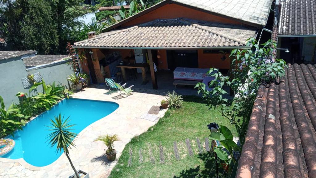 Vista da parte da frente da casa Bem Estar à Beira Mar, uma piscina ampla, um jardim e uma varanda com churrasqueira e um banco de madeira