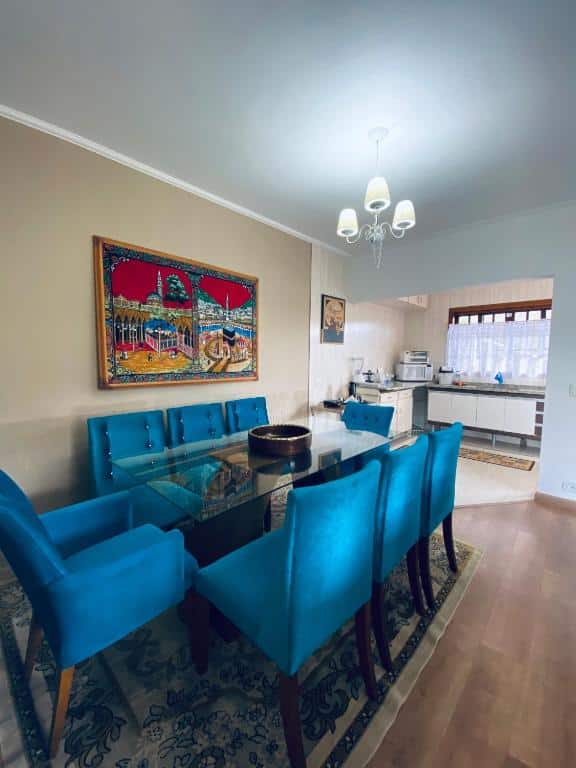 Sala de estar Casa dos Neves, uma mesa com oito lugares, cadeiras azuis, uma cozinha ao lado e uma abajur sob a mesa