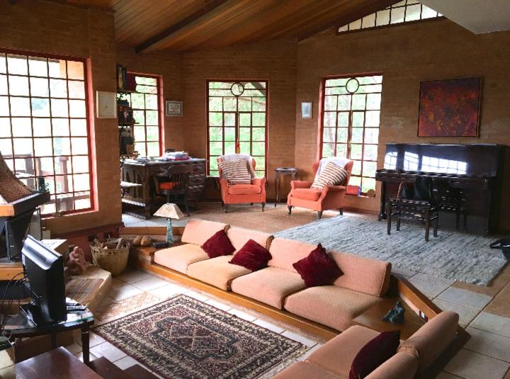 Sala de estar da Casa aconchegante na montanha à 15min do centro, local amplo, um sofá com quatro lugares, uma lareira, duas poltronas, um piano, três janelas grandes, para representar airbnb em Campos de Jordão