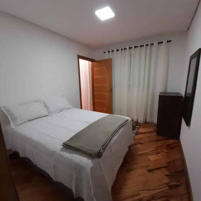 Quarto na Casa Requinte em Campos do Jordão, uma cama de casal, uma espelho, uma cômoda, uma janela com cortina, para representar airbnb em Campos do Jordão