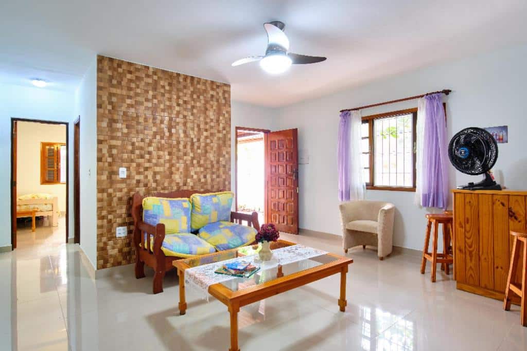 Sala de estar da Casa Ubatuba- praia da Lagoinha, um sofá, alguns bancos, uma poltrona, um ventilador, janela ampla e vista para o quarto, para representar airbnb em Ubatuba